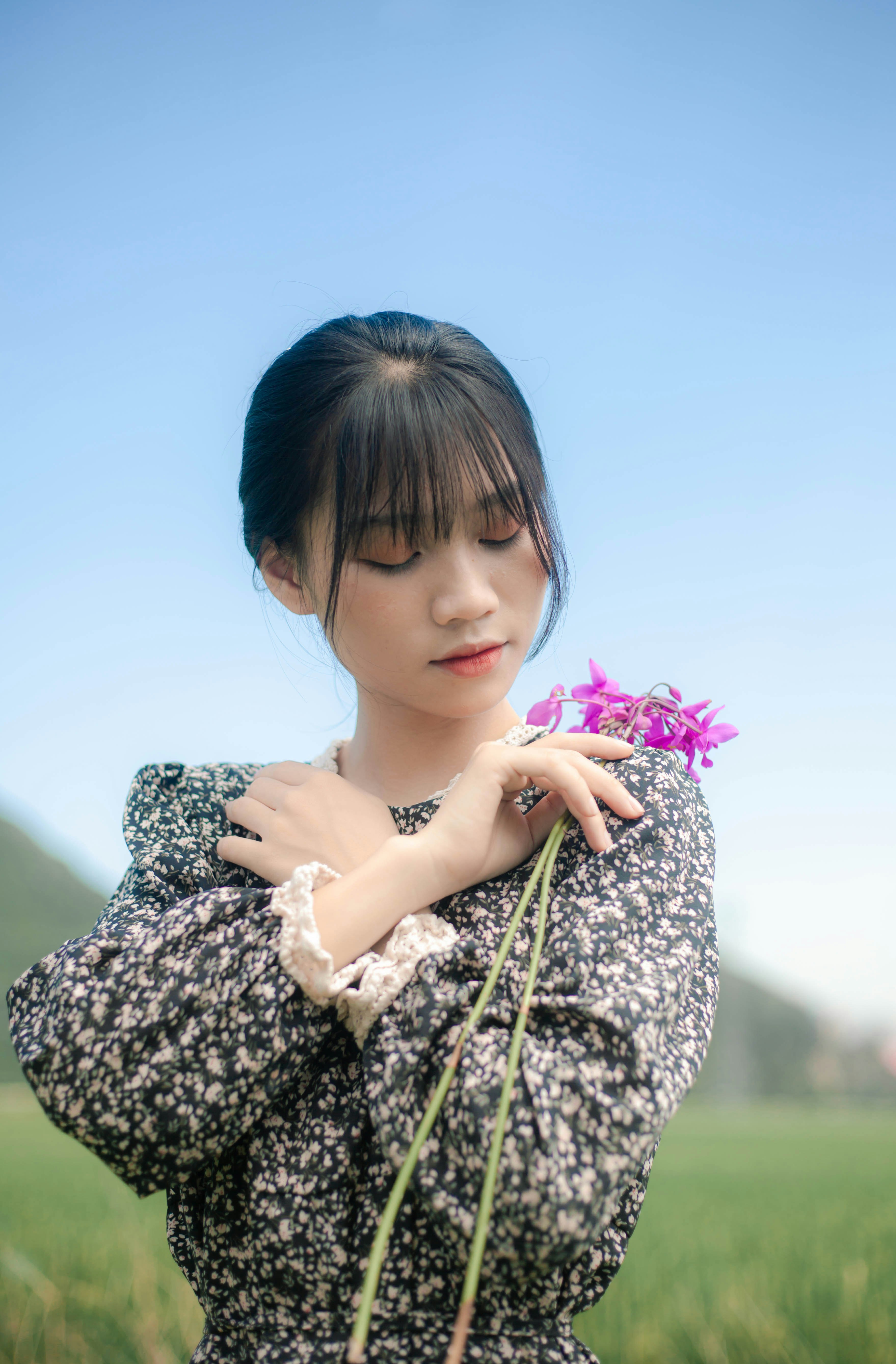 woman in black and white floral dress holding pink flower during daytime